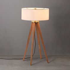 a wooden tripod floor lamp with a white shade on the top and a black cord plugged into it