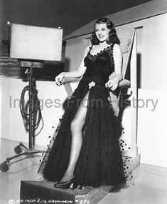 an old photo of a woman in a black dress posing for the camera with her legs spread out