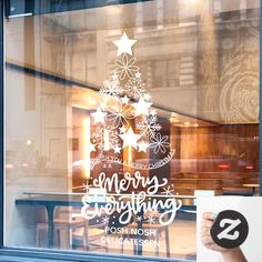 a person holding up a sign in front of a store window that says merry everything