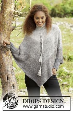 a woman standing next to a tree wearing a gray ponchy