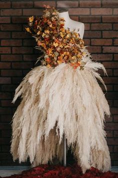 a mannequin is covered with flowers and feathers in front of a brick wall