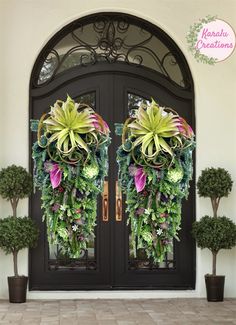 two large wreaths on the front door of a house decorated with flowers and greenery