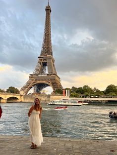 a woman standing in front of the eiffel tower with boats on the water