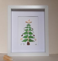 a white frame with a green christmas tree on it and seashells next to it