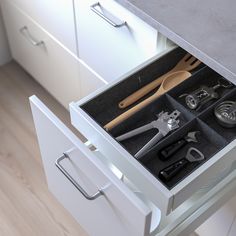 an open drawer with tools and utensils in it on a wooden floor next to white cabinets