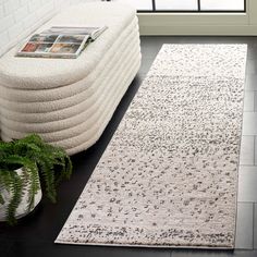 a white rug on the floor next to a couch and potted plant in front of a window