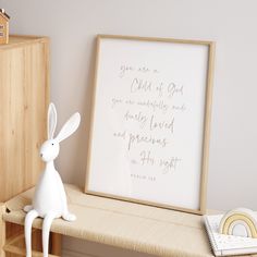 a white rabbit figurine sitting on top of a wooden shelf next to a framed print