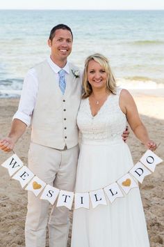 a man and woman are standing on the beach with their arms around each other while holding a banner that says we still do