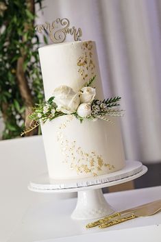 a white wedding cake with gold glitter and flowers on top is sitting on a table