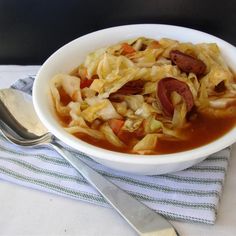 a white bowl filled with noodles and meat on top of a table next to a fork