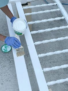 a person in blue gloves is painting a white fence with some paint and a brush