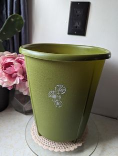 a green flower pot sitting on top of a glass table next to a pink flower