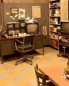 an office with two desks and several televisions on the shelves in front of them