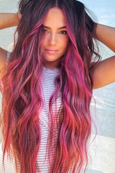 a woman with long, wavy hair and pink ombrees on her head is looking at the camera