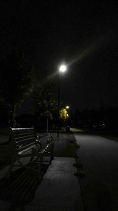 two park benches sitting next to each other on a sidewalk at night under a street light