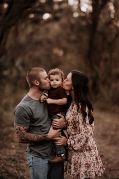 a man and woman kissing their son in the woods