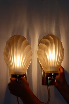 two lamps that have shells on them in the shape of seashells are being held up against a white wall