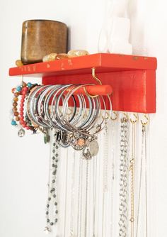 there is a red shelf with many bracelets on it and a white wall in the background