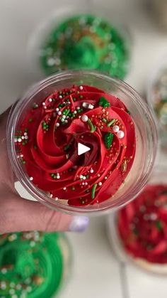 a person is holding a cupcake with red frosting and sprinkles