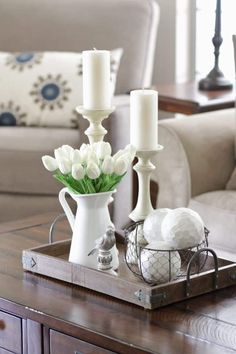 a tray with candles and flowers in it on a table next to a couch or chair