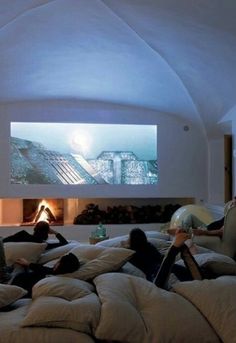 three people laying on pillows in front of a flat screen tv that is mounted to the wall