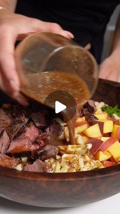 a person pouring dressing on top of a bowl filled with meat, vegetables and fruit