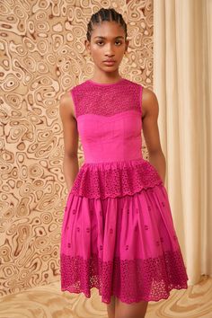 a woman standing in front of a wall wearing a pink dress with lace on it