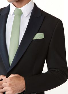 a man in a black suit with a green tie and pocket square on his lapel