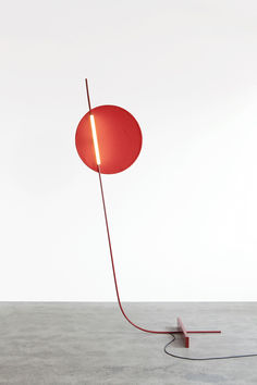 a red lamp sitting on top of a cement floor next to a light fixture with a cord