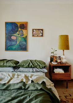 a bed sitting in a bedroom next to a lamp and pictures on the wall above it