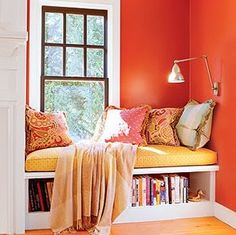 a window seat with pillows and blankets on it next to a book shelf filled with books