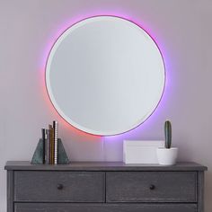 a round mirror sitting on top of a wooden dresser next to a potted cactus