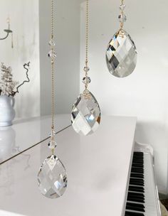 three glass ornaments hanging from strings on a white counter top with a piano in the background