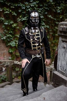 a man wearing a black and gold outfit standing on steps in front of a tree