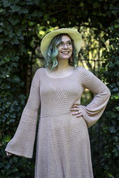 a woman with green hair wearing a tan dress and a yellow hat smiles at the camera