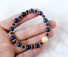 This gold beaded lapis lazuli gemstone bracelet is handmade with gold spacer beads, dark blue lapis gemstones and vintage glass pearl.   I hand selected each smooth round lapis stones, gold beads and glass pearl, and each are set on durable professional stretch elastic cord.  The beaded stone stretch bracelet cord is knotted and glued to secure the knot.  Easy to wear, just slide on and off.   Ideal birthday gift for the special person in your life.  Lapis is the birthstone for September, and 32 Blue Pearl Bracelet With Gemstone Beads As A Gift, Blue Pearl Bracelet With Gemstone Beads For Gift, Lapis Lazuli Beaded Bracelets As Gift, Lapis Lazuli Bead Bracelet Gift, Gold Bracelets With Lapis Lazuli And Natural Stones, Lapis Lazuli Gemstone Beaded Bracelet For Gifts, Lapis Lazuli Gemstone Beads Bracelet For Gift, Gift Lapis Lazuli Round Bead Bracelets, Gift Lapis Lazuli Bracelets With Round Beads