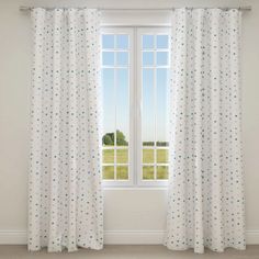 a white curtain with blue polka dots hanging in front of a window overlooking a green field