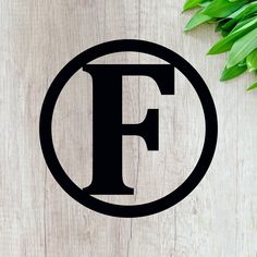 the letter f is in a circle on a wooden surface next to some green leaves