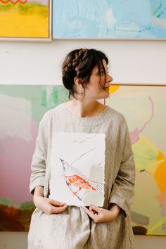 a woman standing in front of paintings holding a piece of paper with an image of a bird on it