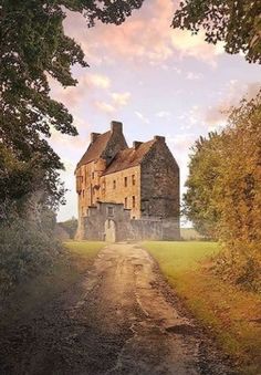 an old castle sitting on the side of a dirt road in front of some trees