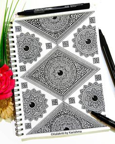 a spiral notebook with black and white designs on the cover next to a red flower