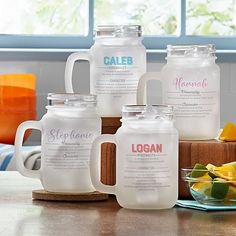 six glass jugs with labels on them sitting on a wooden table next to fruit