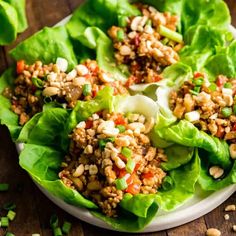 lettuce wraps filled with meat and vegetables on a white plate sitting on a wooden table