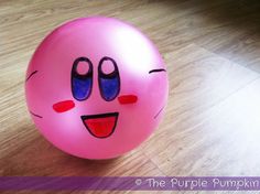 a pink ball with eyes and nose drawn on it sitting on a wooden floor next to a wall