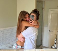 two women are hugging in the kitchen while one takes a selfie with her phone