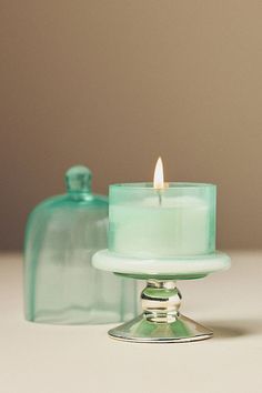 a lit candle sitting on top of a glass cake plate next to a container with a lid