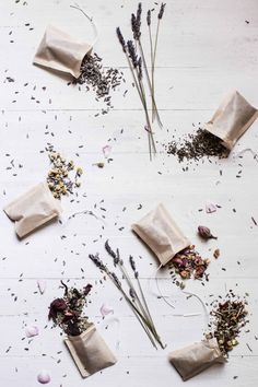 dried flowers and herbs are laid out on a white wooden surface, with paper bags in the middle