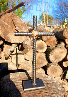 a metal cross sitting on top of a piece of wood next to some cut logs