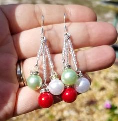 a person is holding three different colored beads in their hand and wearing earrings with chains