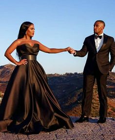 a man and woman in formal wear hold hands as they stand on top of a hill